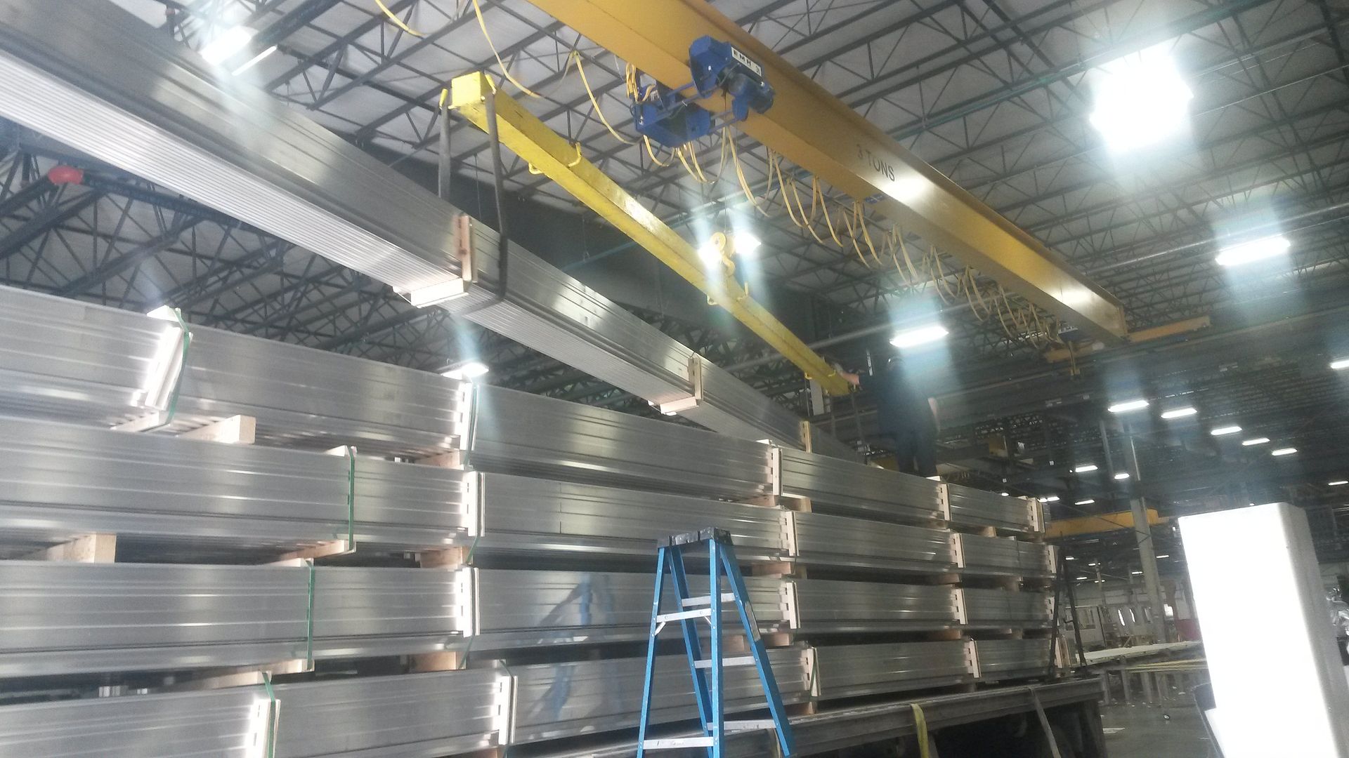 Overhead crane loading aluminum onto a flatbed truck indoors.